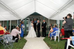 A bride and groom standing at the altar under a white tent during an outdoor wedding ceremony.
