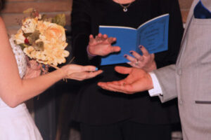 A bride and groom exchange wedding rings held by an officiant.
