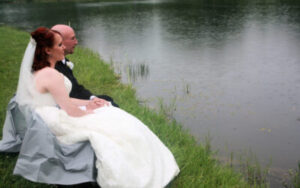 A bride and groom sitting by a pond in the rain.