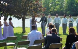 A couple exchanging vows at an outdoor wedding ceremony in front of a wedding party and guests.