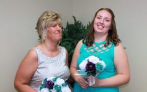 Two women in formal dresses holding bouquets of white and purple flowers.