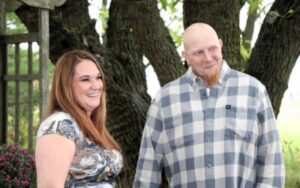 A woman with long hair smiling next to a man with a goatee in a plaid shirt.