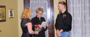 An officiant reads from a document during a wedding ceremony as a couple stands before her.