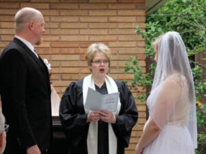 A wedding officiant in a robe performs a ceremony for a bride and groom.