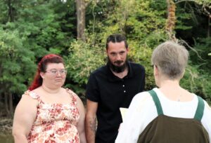 A couple stands before an officiant outdoors.