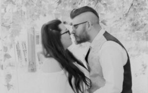 A couple in wedding attire face each other closely under tree branches.