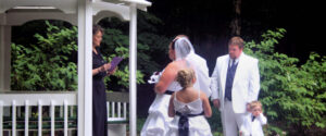 An officiant leads a wedding ceremony for a bride and groom, with a flower girl and a ring bearer standing nearby.
