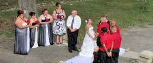 A bride and groom exchange vows at an outdoor wedding ceremony, surrounded by their bridal party.