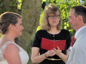 An officiant reading from a red book during a wedding ceremony between a bride and groom.