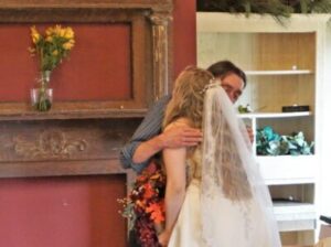 A bride in a wedding dress and veil embraces a man indoors.